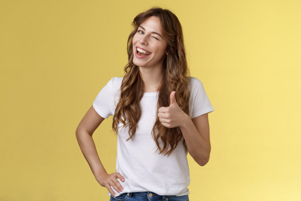 I support you guys good luck. Happy cheerful cheeky attractive girl wink approval like show thumb up smiling broadly satisfied awesome party congratulating friend well done yellow background.