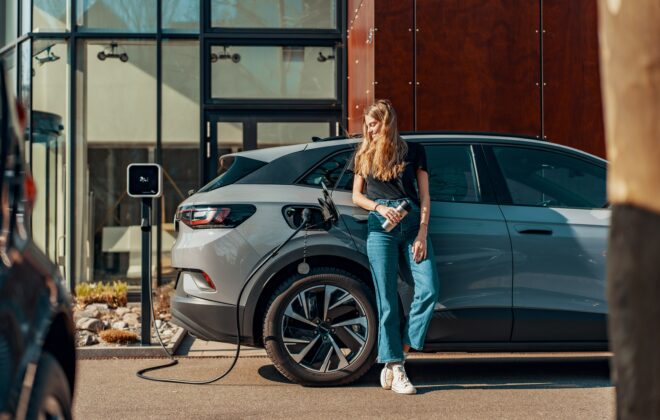 Une femme rechargeant sa voiture électrique via une borne de recharge sur pied de fixation.